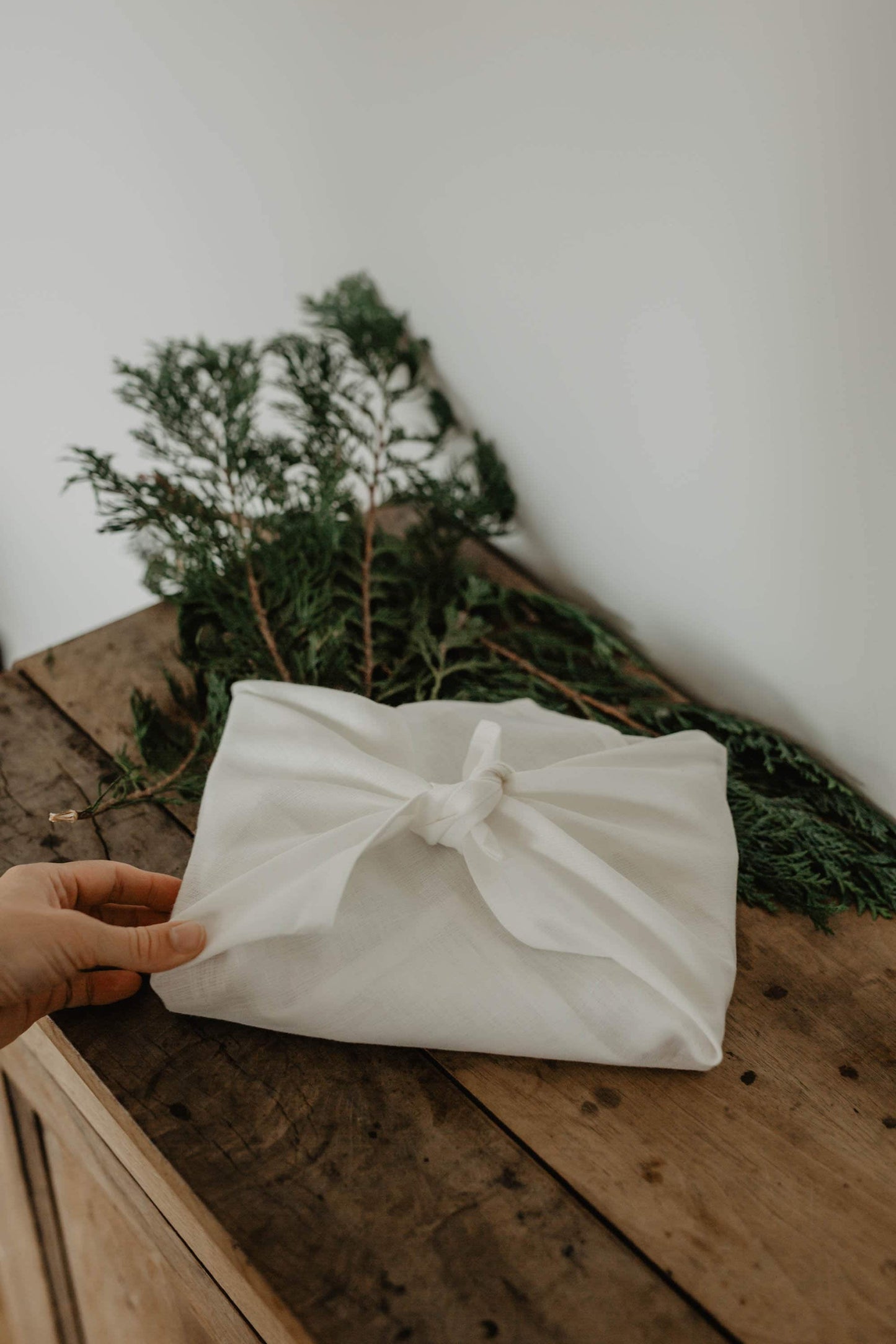 present wrapped in white linen furoshiki wrapping with branch