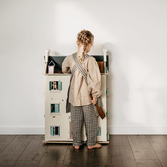 Child with linen clothes playing with a doll house