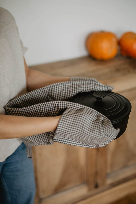 linen double oven mitt holding a hot pot next to cupboard